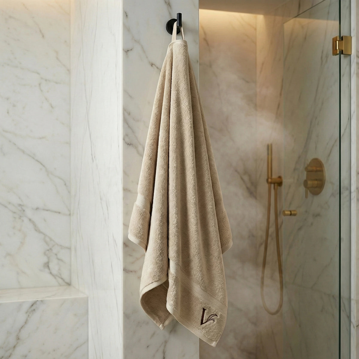 Velioni Saunatuch in Beige hängt an einem Haken in luxuriösem Marmorbad mit goldener Regendusche und Glasabtrennung