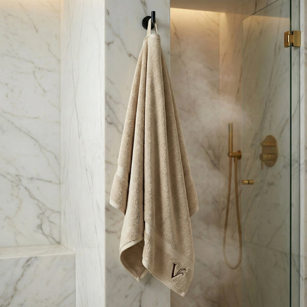 Velioni Saunatuch in Beige hängt an einem Haken in luxuriösem Marmorbad mit goldener Regendusche und Glasabtrennung